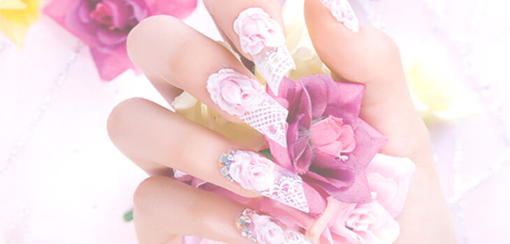 Hand mit außergewöhnlich gut designten Fingernägeln. Im Hintergrund ein paar Blüten.